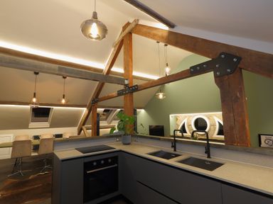 A kitchen area with a sink and oven next to a dining area under a ceiling with wooden beams at The Sigma Penthouse in Dyserth