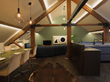 An open space attic room with a dining table and chairs on the left and a kitchen island on the right at The Sigma Penthouse in Dyserth