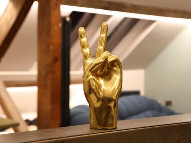 A golden hand sculpture showing a peace sign on a shelf in a room with wooden beams and a blue couch at The Sigma Penthouse in Dyserth
