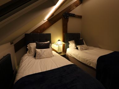A bedroom with two single beds a bedside table with a lamp and exposed wooden beams at The Sigma Penthouse in Dyserth