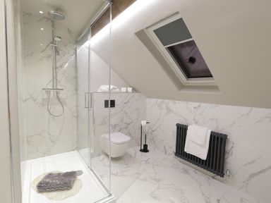 A bathroom with a glass shower enclosure a wall-mounted toilet a towel radiator under a skylight at The Sigma Penthouse in Dyserth