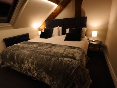 A bedroom with a large bed bedside table with lamp and exposed wooden beams at The Sigma Penthouse in Dyserth