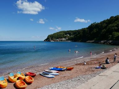 A beach with kayaks and paddleboards on the shore and people in the water at Saltwater Cottage in Babbacombe