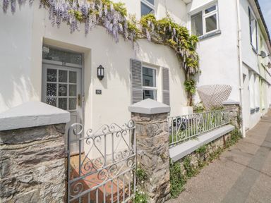 The exterior of a white house with a gray door and window shutters a small garden with purple flowers and a stone and metal fence at Saltwater Cottage in Babbacombe