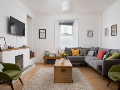 A living room with a gray sectional sofa with colorful pillows a wooden coffee table with flowers and two green armchairs at Saltwater Cottage in Babbacombe
