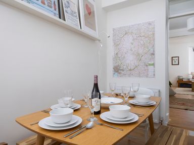A dining table set with white bowls plates glasses and cutlery with a bottle of wine on the table at Saltwater Cottage in Babbacombe