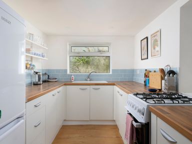 A kitchen with white cabinets wooden countertops gas stove and a window over the sink at Saltwater Cottage in Babbacombe