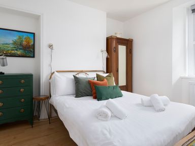 A bedroom with a bed with pillows and rolled towels a green dresser a wooden wardrobe and a painting at Saltwater Cottage in Babbacombe