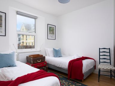 A bedroom with two single beds red blankets and blue pillows with a chair and framed pictures on the wall at Saltwater Cottage in Babbacombe