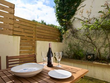 An outdoor wooden table with plates wine bottle and glasses next to a wooden fence and plants at Saltwater Cottage in Babbacombe