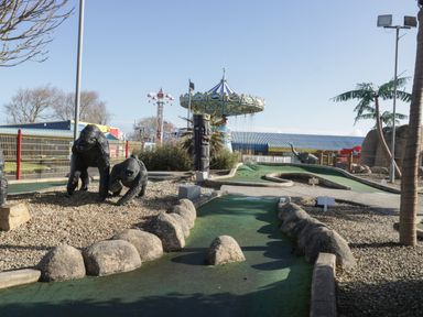 An outdoor mini golf course with gorilla statues and a carousel ride in the background at 14 Fairways in Burnham-On-Sea
