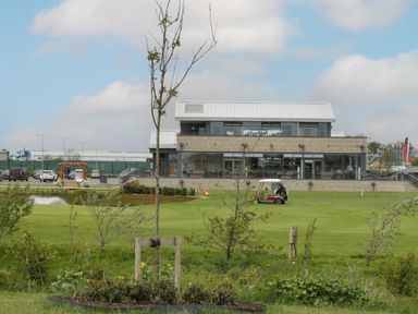 A golf course with a golf cart and a modern building in the background at 14 Fairways in Burnham-On-Sea
