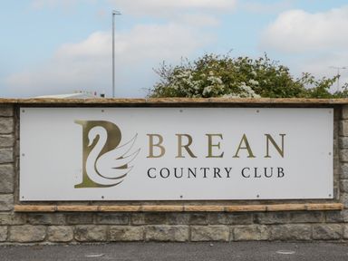 A stone wall with a sign that reads Brean Country Club with a swan logo