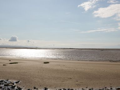 A sandy beach with water and sparse grass patches under a partly cloudy sky at 14 Fairways in Burnham-On-Sea