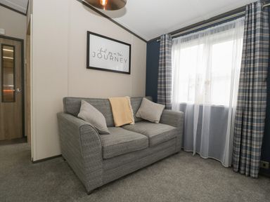 A living room with a grey sofa cushions blanket plaid curtains and a framed quote at 14 Fairways in Burnham-On-Sea