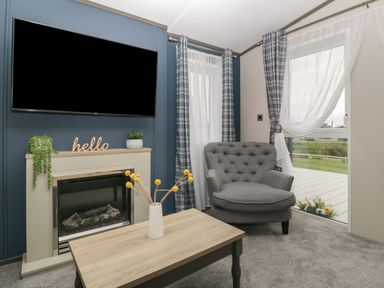 A living room with a fireplace a wall mounted television a gray armchair and a wooden coffee table at 14 Fairways in Burnham-On-Sea