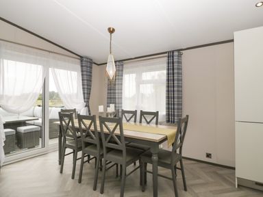 A dining area with a rectangular table and eight chairs near windows with plaid curtains and sheer white drapes at 14 Fairways in Burnham-On-Sea