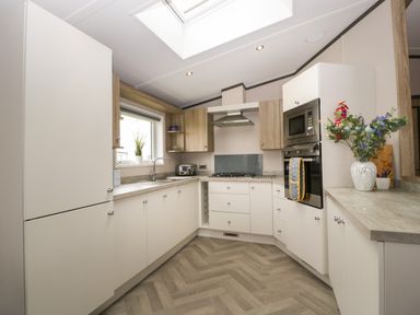 A kitchen with white cabinets a stove microwave and a vase of flowers on the counter at 14 Fairways in Burnham-On-Sea
