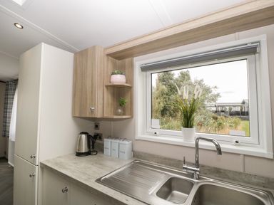 A kitchen countertop with a stainless steel sink kettle canisters and potted plants by a window at 14 Fairways in Burnham-On-Sea
