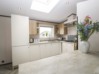 A kitchen with white and wood cabinets a window over the sink and a vase with flowers on the counter at 14 Fairways in Burnham-On-Sea