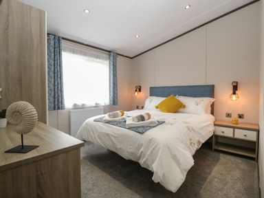 A bedroom with a bed with two rolled towels bedside tables and a dresser at 14 Fairways in Burnham-On-Sea