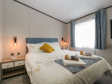 A bedroom with a bed side table and window with curtains at 14 Fairways in Burnham-On-Sea