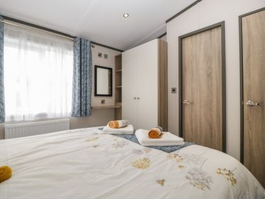 A bedroom with a bed towels on it a wardrobe a mirror and blue patterned curtains at 14 Fairways in Burnham-On-Sea