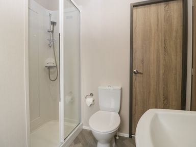 A bathroom with a shower enclosure a toilet a wooden door and a sink at 14 Fairways in Burnham-On-Sea