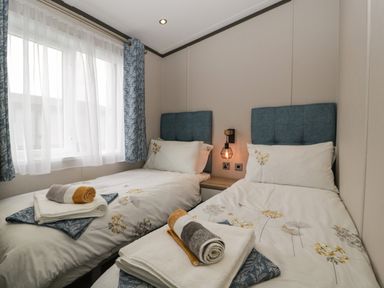 A bedroom with two single beds and rolled towels on each bed by a window at 14 Fairways in Burnham-On-Sea