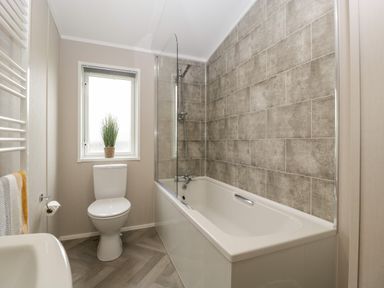 A bathroom with a bathtub and shower next to a window and a toilet at 14 Fairways in Burnham-On-Sea