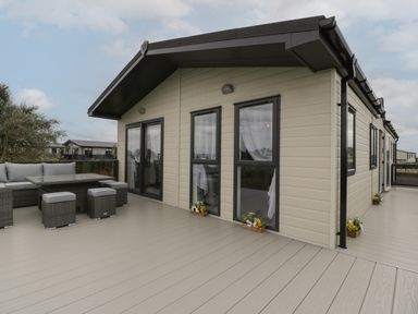 Exterior view of a beige modular home with black-framed windows and patio furniture on a wooden deck at 14 Fairways in Burnham-On-Sea