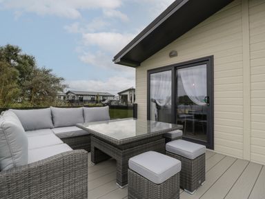 An outdoor patio with a wicker sofa set a glass table and a sliding glass door at 14 Fairways in Burnham-On-Sea