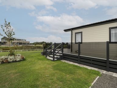 An outdoor view of a house with a raised deck surrounded by glass railing and a lawn with a small landscaped garden at 14 Fairways in Burnham-On-Sea