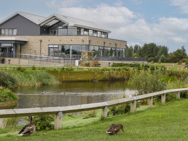 A pond with ducks in front of a modern building and a wooden fence at 14 Fairways in Burnham-On-Sea