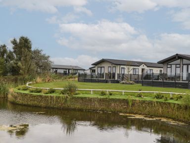 A view of houses near a pond with grass and trees at 14 Fairways in Burnham-On-Sea