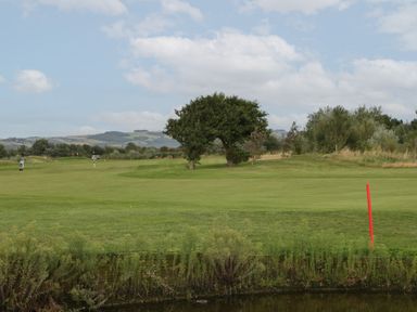 A golf course with trees and a pond with hills in the background at 14 Fairways in Burnham-On-Sea