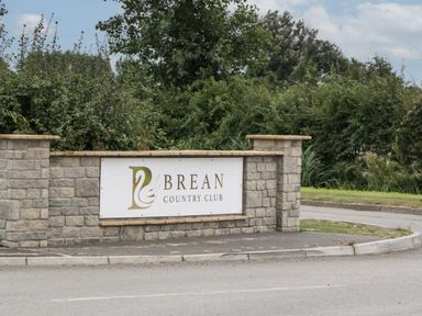 A stone wall sign for Brean Country Club surrounded by bushes and trees