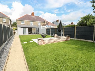A backyard with green grass a paved walkway black fence two black chairs and a house in the background at Larkhill in Tenby