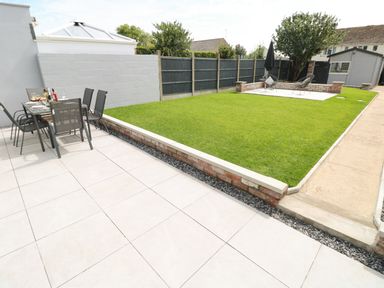 A backyard with tiled patio table and chairs a lawn a paved seating area and a garden shed at Larkhill in Tenby
