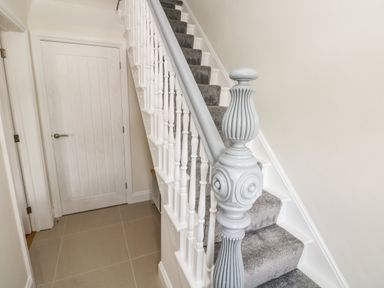 A staircase with grey carpet and a white painted banister next to a closed white door at Larkhill in Tenby