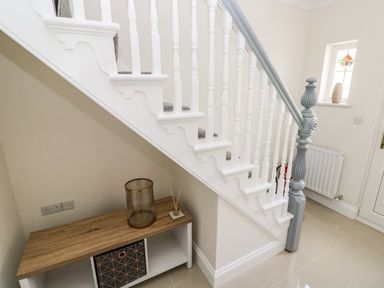 A staircase with white balusters and a gray handrail with a small wooden cabinet underneath at Larkhill in Tenby