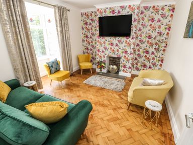 A living room with green and yellow chairs a floral wallpaper and a wall mounted tv at Larkhill in Tenby