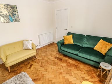 A living room with a green sofa with yellow cushions a yellow loveseat with a silver cushion a small round side table and a peacock painting on the wall at Larkhill in Tenby