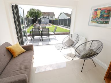 A living area with a sofa and two chairs with cushions leading to an outdoor dining table and garden at Larkhill in Tenby