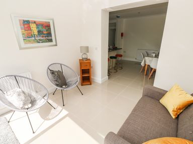A living room with two round chairs with cushions a small wooden side table with lamp and a brown sofa with yellow cushions at Larkhill in Tenby