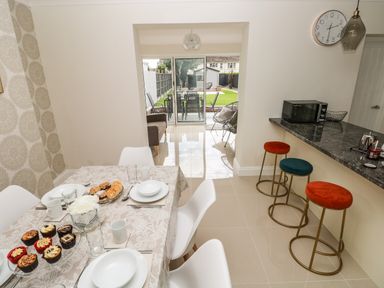 A dining area with a table set with cupcakes and plates adjacent to a kitchen counter with stools and a garden visible through glass doors at Larkhill in Tenby