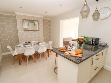 A dining area with a table set for six and a kitchen island with bread flowers and a microwave at Larkhill in Tenby