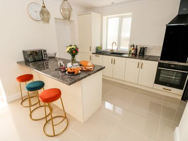 A kitchen with a countertop island and three stools a microwave and a vase with flowers on the countertop at Larkhill in Tenby