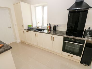 A kitchen with white cabinets black countertop black sink oven and stove at Larkhill in Tenby