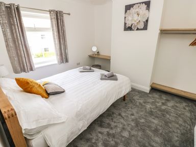 A bedroom with a bed made with white linens and two towels on it next to a window with curtains and a wall with a floral painting at Larkhill in Tenby